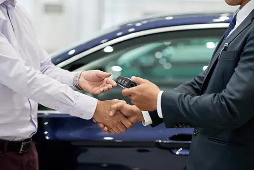 Businessman in a suit takes the key for his new car from the dealer